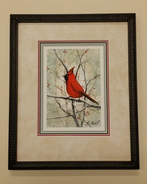 A P. Buckley Moss print of a red cardinal on a snowy branch, framed in a carved black frame with a wide linen mat and thin red, black and grey inner mats
