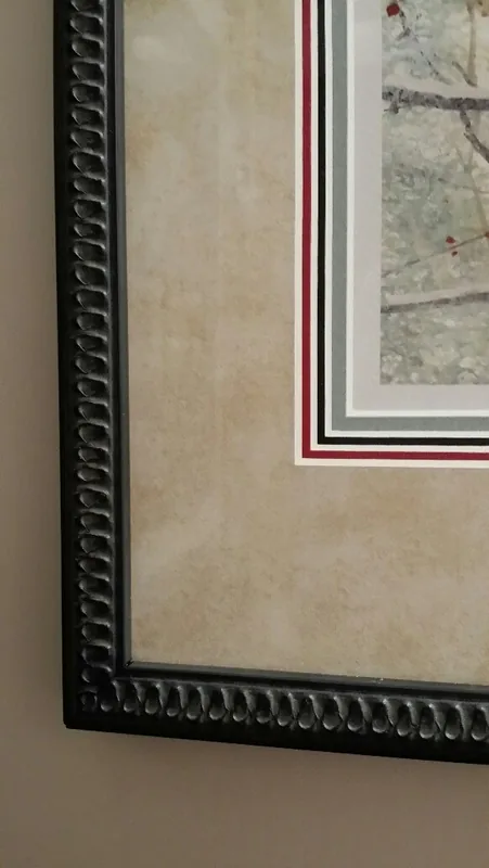 Close up of a frame corner: a carved black wooden frame, a wide linen colored mat, then thin red, black and grey mat reveals around a print of a cardinal in snow