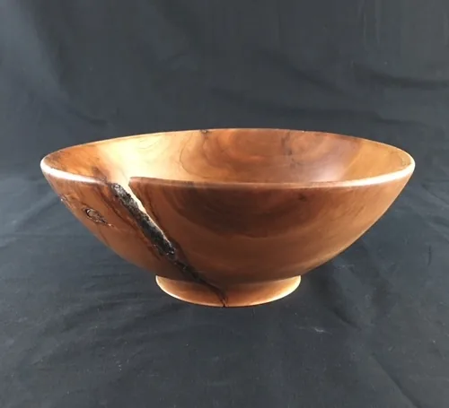 A hand turned wooden bowl with warm reddish grain on a black background